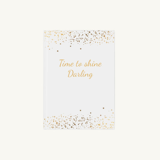 Weißes A5 Notizbuch mit der Aufschrift 'Time to shine Darling' in goldener Schrift mit kleinen goldenen Sternen für die Menopause. Das Journal ist als Begleiter für Achtsamkeit und Reflexion für Frauen in den Wechseljahren konzipiert.