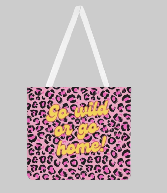 Stylische Stofftasche mit auffälligem pink-schwarzem Leopardenmuster. In der Mitte steht der gelbe Schriftzug 'Go wild or go home!' in einer verspielten Schriftart. Die Tasche hat weiße Tragehenkel und ist vor einem grauen Hintergrund freigestellt.