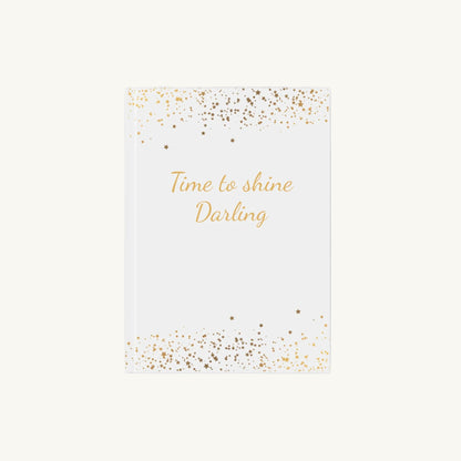 Weißes A5 Notizbuch mit der Aufschrift 'Time to shine Darling' in goldener Schrift mit kleinen goldenen Sternen für die Menopause. Das Journal ist als Begleiter für Achtsamkeit und Reflexion für Frauen in den Wechseljahren konzipiert.