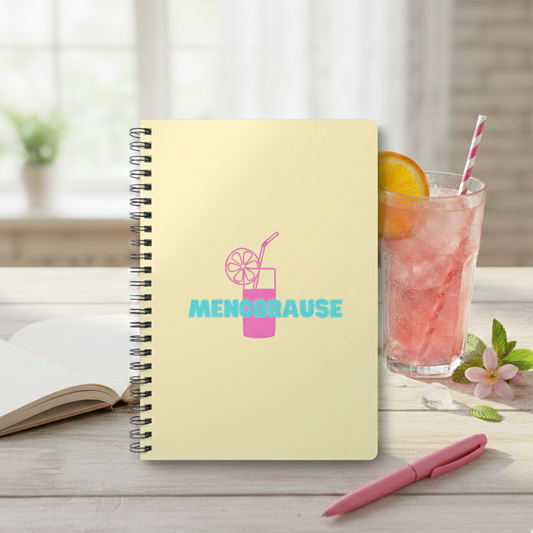 Gelbes A5 Spiralnotizbuch mit der Aufschrift 'MENOBRAUSE' in blauer Schrift und einer pinken Illustration eines Erfrischungsgetränks mit Strohhalm und Zitrone. Lustiges Journal-Design für Frauen in den Wechseljahren,was von einem Glas mit Strohalm und hinter einem rosa Kugelschreiber steht