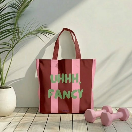 Hochwertige Tote Bag in Burgund und Rosa mit dem grünen Statement-Aufdruck „Uhhh, Fancy“ von HOOHAA, mit zwei kleine rosa Hanteln in hellen, sonnigen Raum mit Palmenschatten.