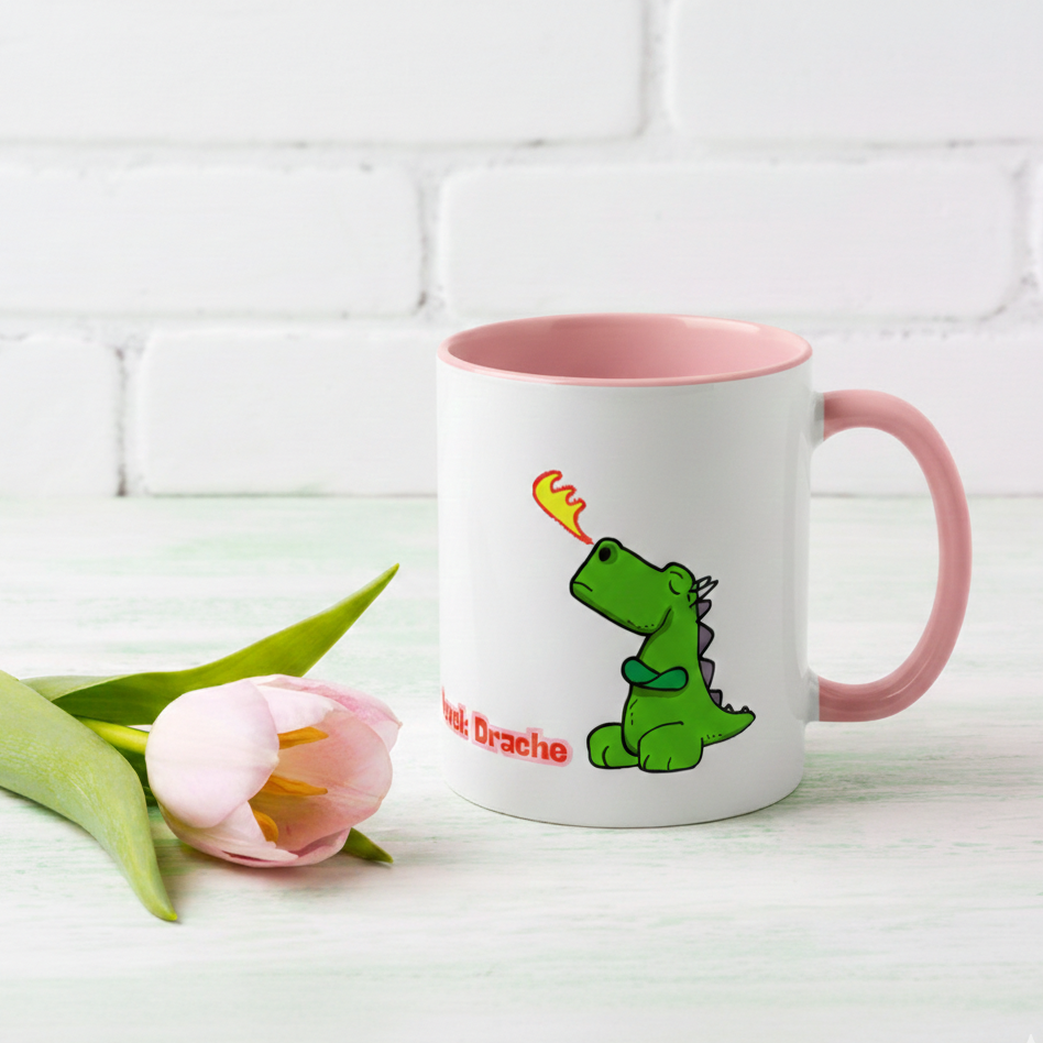 Weiße Keramiktasse mit rosa Henkel und Innenseite, illustriert mit einem kleinen grünen Drachen, der Feuer speit, und dem pinken Schriftzug „Hormonlevel: Drache“ die neben einer rosa Tulpe auf einem Tisch steht