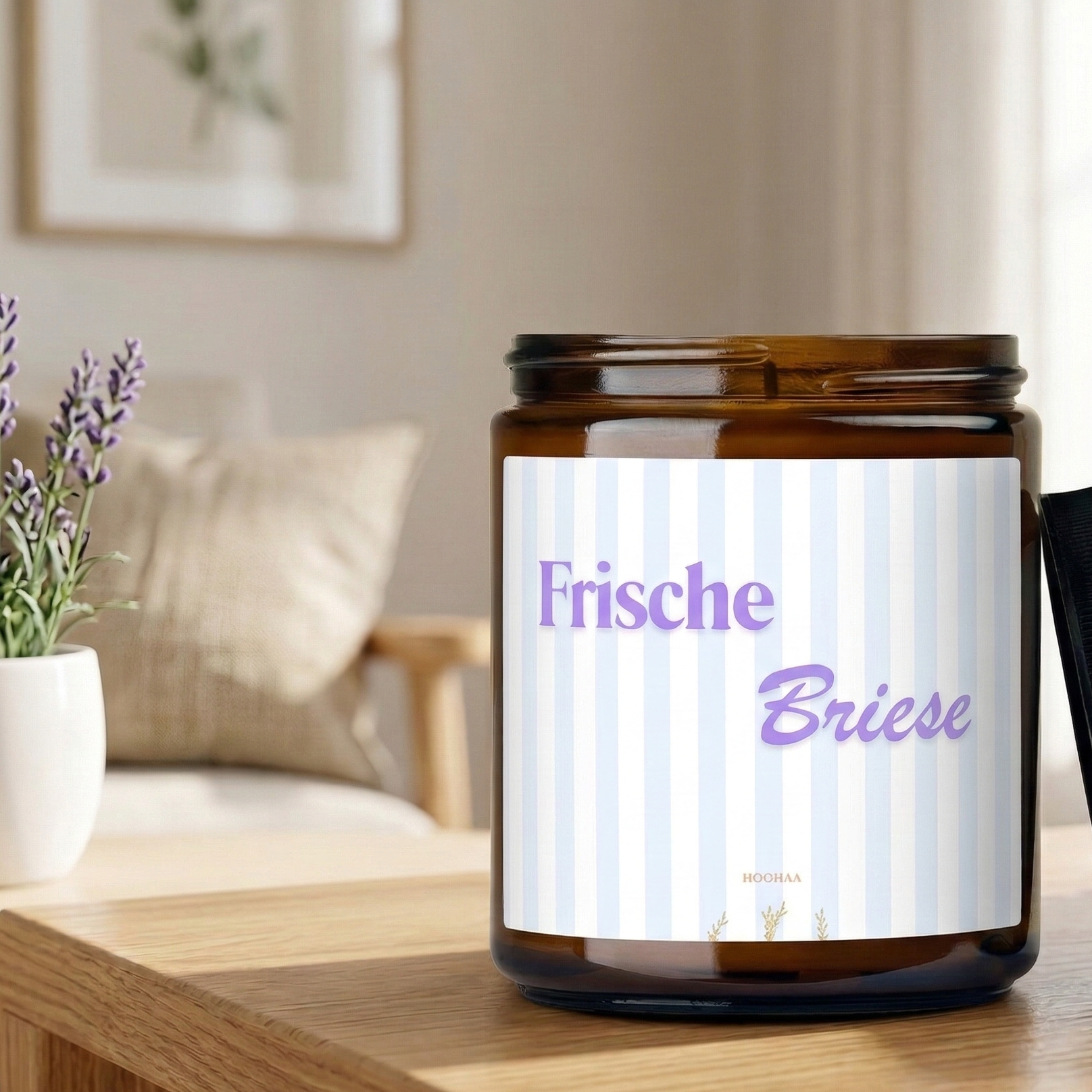 Hochwertige handgefertigte Sojawachs-Duftkerze „Frische Briese“ in einem Braunglas, hergestellt in Berlin, mit blau-weiß gestreiftem Etikett und schwarzem Deckel, steht auf einem hellen Holztisch neben einem Topf Lavendel in einer gemütlichen Wohnzimmeratmosphäre.