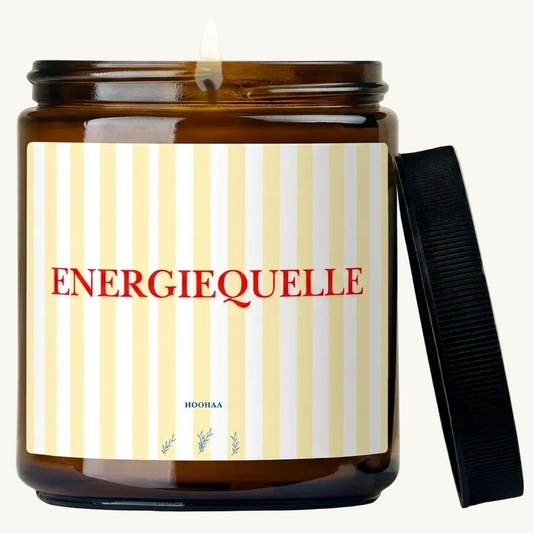 Mockup einer handgefertigten Sojawachskerze im Braunglas mit gelb-weiß gestreiftem Etikett und dem roten Schriftzug „Energiequelle“, platziert in einer hellen Wand