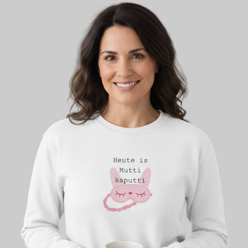 Weißes Damen-Sweatshirt mit Rundhalsausschnitt für Frauen in den Wechseljahren. In der Mitte ist eine geschlossene rosa Schlafmaske mit Augen, Text in schwarzer Schrift 'Heute ist Mutti kaputti' von einer dunkelhaarigen Frau getragen, die ein Tasse in der Hand hält
